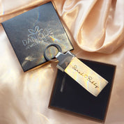Personalized large leather keychain loop in ivory cream color engraved with “Sarah ♥ Bobby,” displayed in a black gift box beside a Danique Jewelry & Gifts branded box on soft satin fabric. This custom leather keychain makes a romantic gift for couples, perfect for anniversary, long distance relationship gift, or Valentine’s Day present. Ideal for boyfriend or girlfriend gifts with engraved names or coordinates. Durable stitched leather key ring accessory for everyday use or sentimental keepsake.