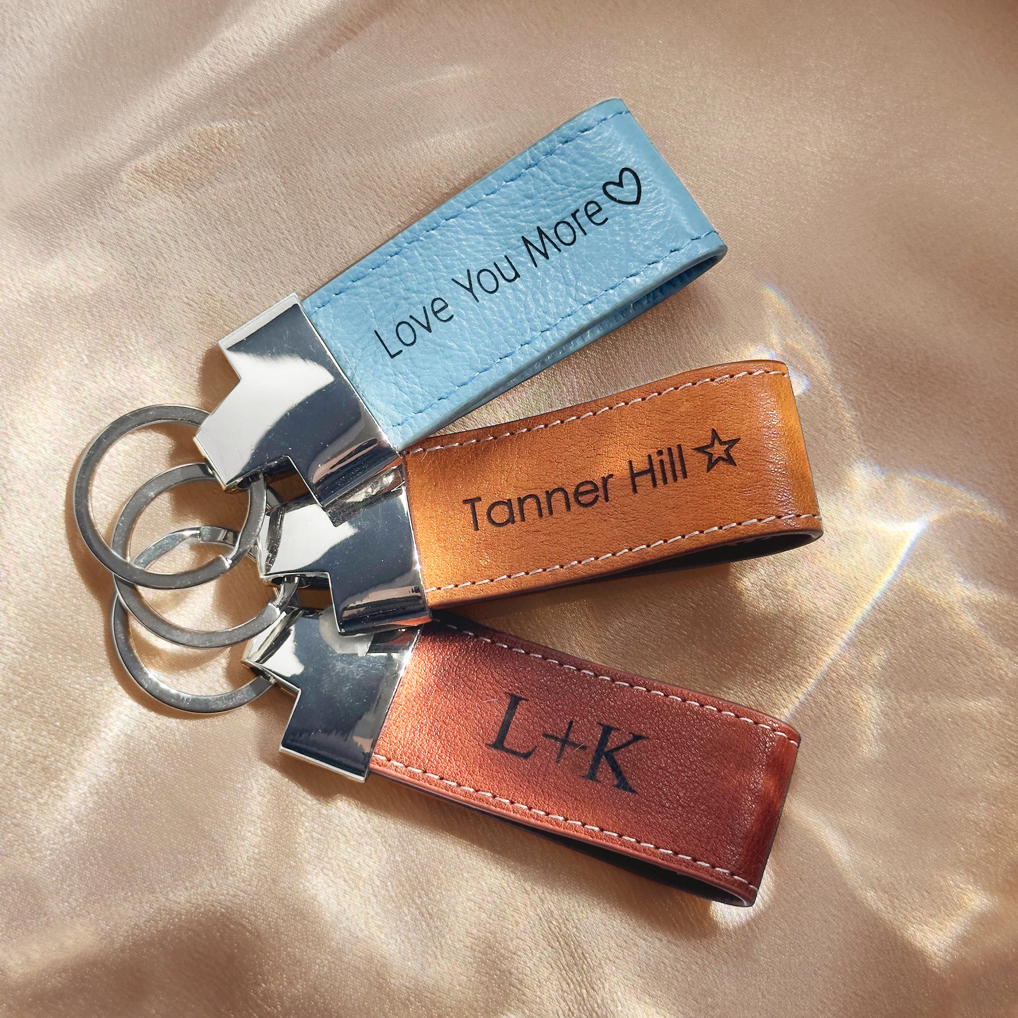 A trio of personalized leather loop keychains featuring engraved coordinates and heartfelt messages “I love you” and custom initials, shown on a natural stone background. These durable leather fobs with stitched edges and silver key rings make thoughtful location-based gifts, GPS memory keepsakes, or sentimental anniversary souvenirs. Handmade from premium full-grain cowhide in a Boston studio—ideal for couples, graduates, or travelers looking to carry a meaningful little piece of memory with their keys.