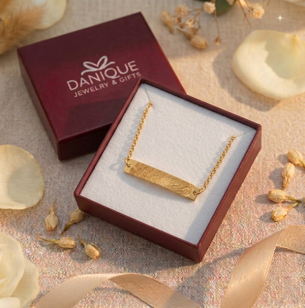 Gold fingerprint bar bracelet displayed in an open red Danique Jewelry gift box with dried floral accents.