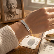 Sterling silver fingerprint memorial bracelet worn beside a framed portrait, fingerprint paper, and remembrance note.