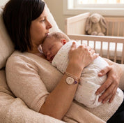Mother holding baby while wearing personalized footprint bracelet, custom newborn keepsake jewelry with baby name and birth date.