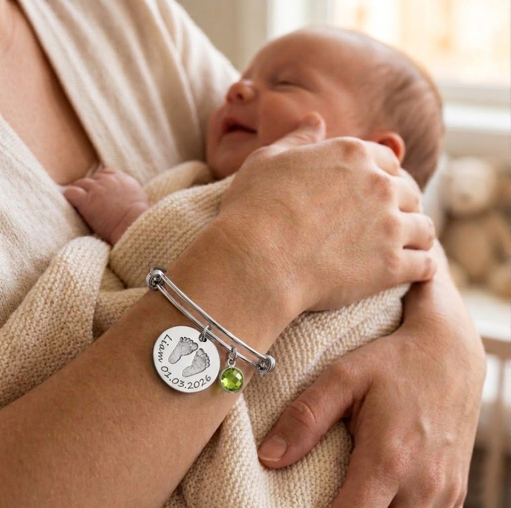 New mom holding baby while wearing custom baby footprint bracelet, a sentimental birthstone bangle gift for mothers and grandmothers.