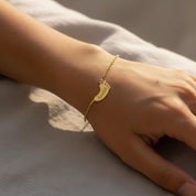 Minimal gold footprint charm bracelet with engraved names and tiny birthstones, worn on wrist; personalized family jewelry for everyday wear and meaningful gift for mom or grandmother.