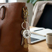 Personalized baby handprint keychain engraved with a real child’s handprint, name, and birth date, shown attached to a brown leather handbag with keys for everyday use. This custom stainless steel baby handprint keychain is a meaningful keepsake gift for a new mom, grandma, or parent, capturing a child’s print in a timeless design. Ideal as a Mother’s Day gift, baby keepsake, or sentimental memorial jewelry, gift-ready and handcrafted in the USA.