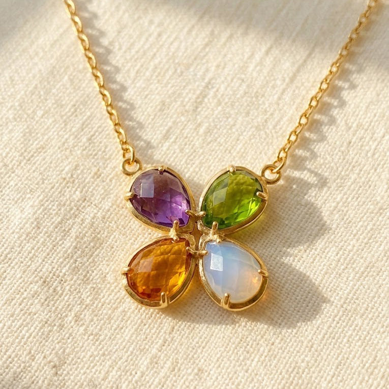 Four birthstone necklace with purple, green, citrine and moonstone teardrop gemstones clustered on a delicate gold chain.
