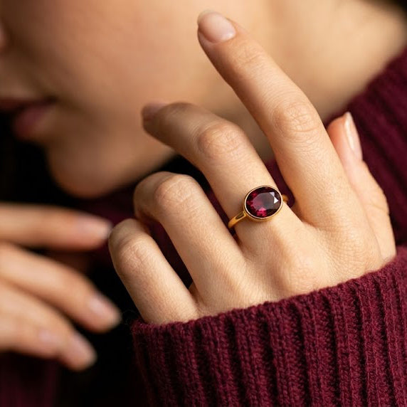 Model wearing oval garnet ring, bezel set red gemstone solitaire; slim stacking band for daily wear; January birthstone jewelry in gold vermeil; elegant minimalist ring ideal for birthday, anniversary, Valentine’s Day or Christmas gift; handcrafted USA; available in sterling silver, rose gold plated, and yellow gold finishes; stackable with other gemstone rings.