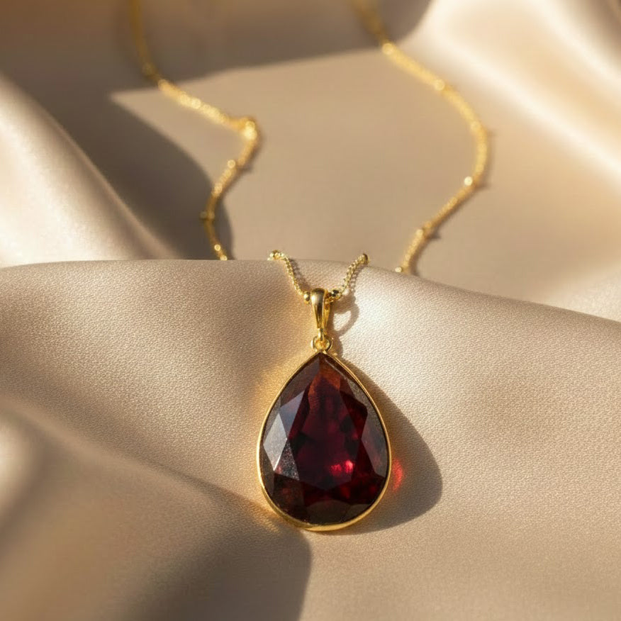 Close up of garnet teardrop January birthstone necklace on satin background