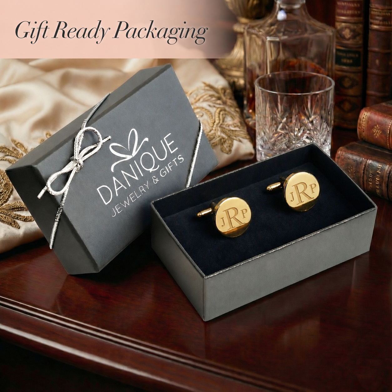 Gold cufflinks in a black box with 'DANIQUE Jewelry & Gifts' packaging on a wooden surface.