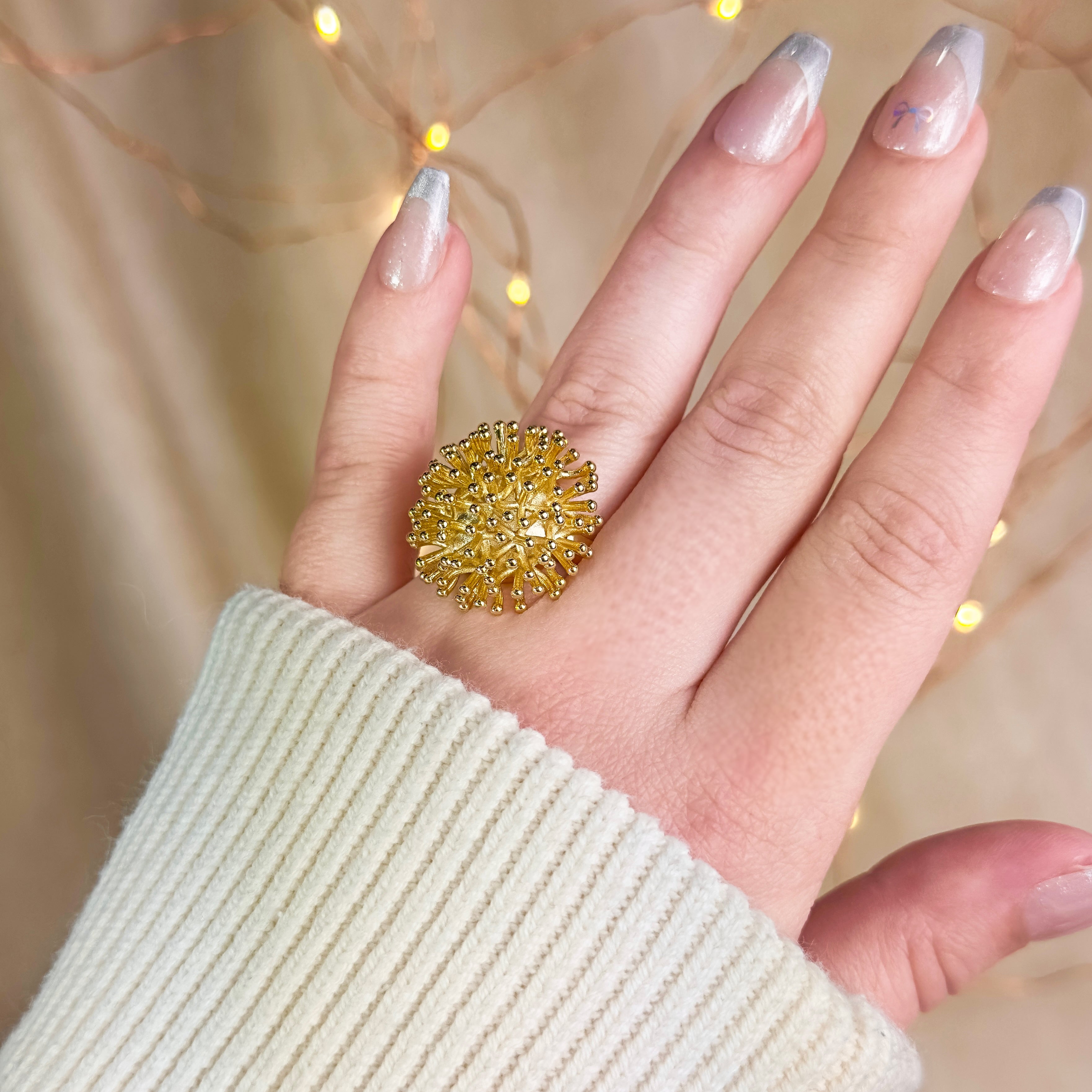 Model wearing a gold burst explosion statement ring - one size. fits sizes 7 and up, silver and gold plating. bold ring, boho ring, statement jewelry, gold statement ring, yellow gold dandelion puff ring, floral ring, nature inspired ring, big flower ring, lightweight statement ring for women, adjustable sretch ring for her