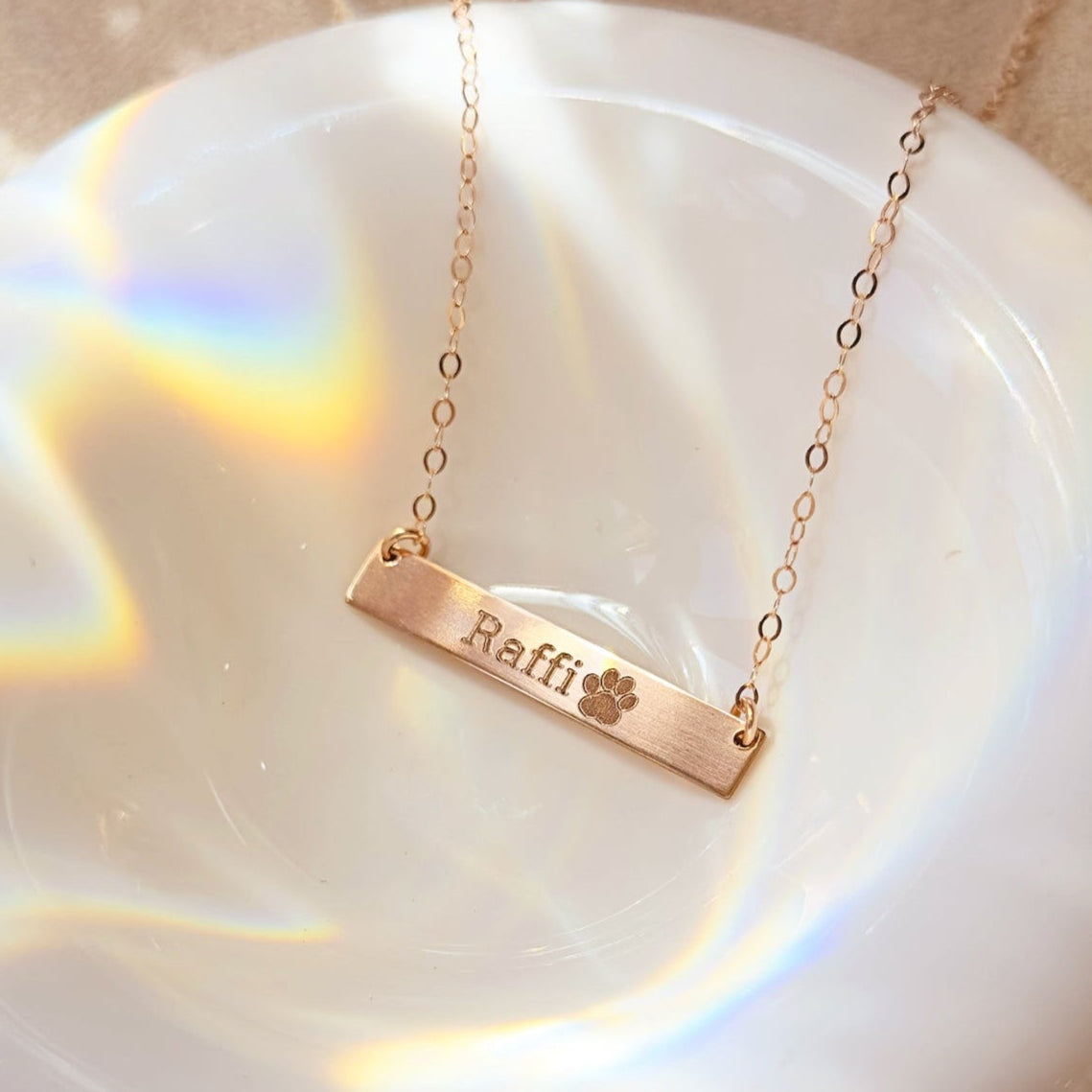 Gold bar paw print necklace with engraved paw print and name "Raffi" in modern font. Personalized pet jewelry made from actual pet paw print, ideal gift for pet lovers, dog moms, and cat owners. Custom gold-filled pendant necklace for birthdays, memorial keepsake, or everyday wear. Includes elegant chain, premium finish, and ready-to-gift packaging.