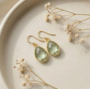 Minimalist green amethyst teardrop earrings with faceted prasiolite gemstone in gold setting, delicate drop earrings styled on neutral background.