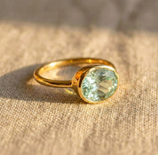 Green amethyst oval bezel set ring photographed at angle, February birthstone gemstone ring with smooth gold band, minimalist fine jewelry for women