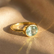 Green amethyst oval bezel set ring in 18K gold vermeil, minimalist February birthstone ring photographed on neutral fabric, dainty gemstone ring for women, elegant everyday jewelry gift