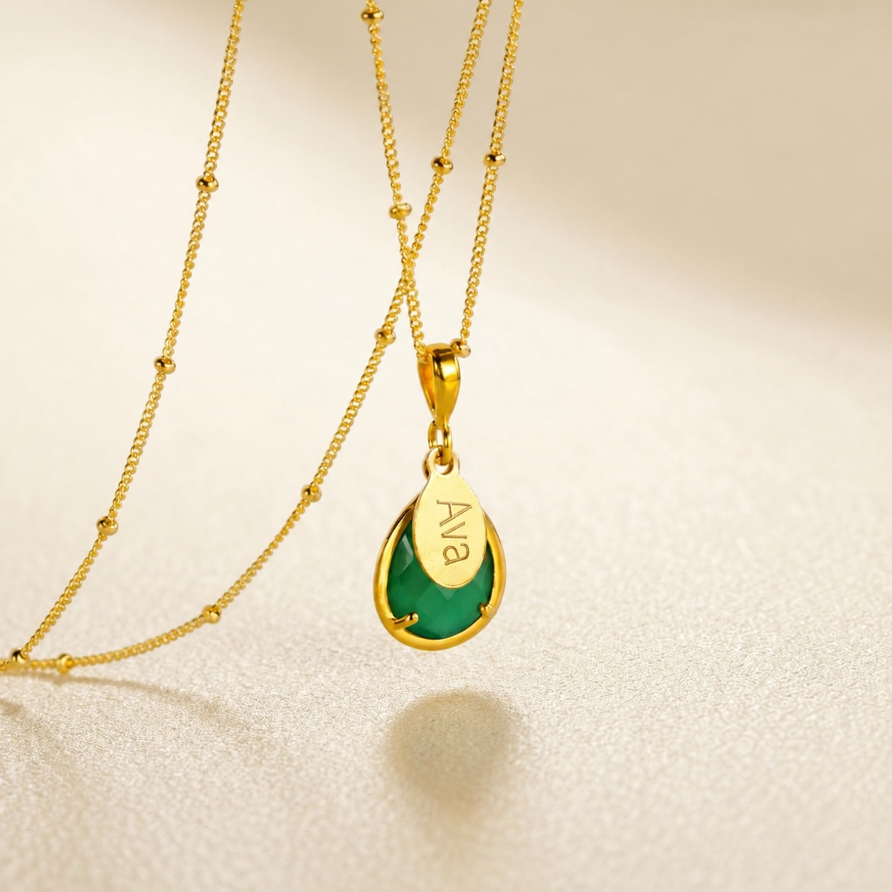 Personalized Green Onyx May birthstone necklace with faceted teardrop gemstone and engraved oval name charm in gold.
