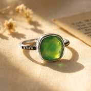 Sterling silver cushion-cut green onyx ring with clear pavé stones on warm beige fabric.