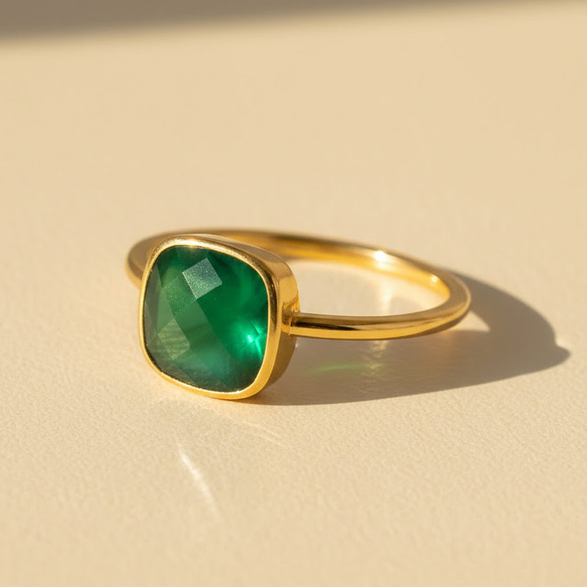 Cushion cut green onyx ring in polished yellow gold bezel setting resting on soft neutral linen fabric, featuring a 9mm square deep emerald green gemstone with smooth glossy finish, minimalist modern statement ring for women, bold gold stacking gemstone ring, handcrafted artisan fine jewelry, square bezel set green onyx ring gift for her