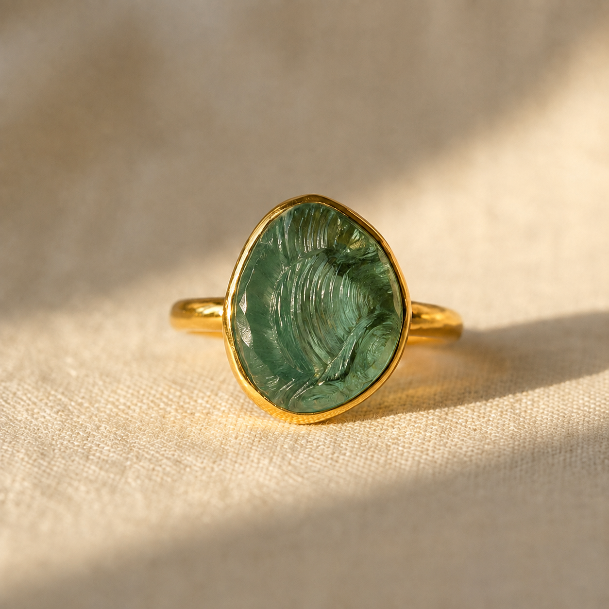 Rough-cut green tourmaline teardrop ring in yellow gold vermeil displayed on warm beige linen.