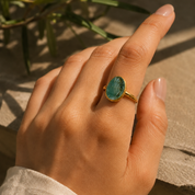 Gold organic teardrop green tourmaline ring worn on a hand in warm natural sunlight.