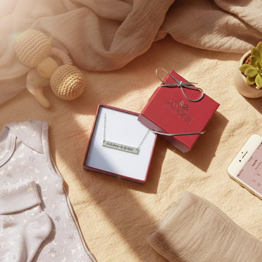 Personalized heartbeat bar necklace in sterling silver displayed in a red Danique Jewelry gift box, styled with soft baby essentials and warm natural lighting, symbolizing a meaningful gift for new mom, baby keepsake, or Mother’s Day jewelry.