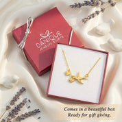 Gold mama bird necklace with baby bird charms displayed in a Danique Jewelry gift box on soft fabric with lavender accents. Personalized family necklace packaged for gifting, perfect meaningful gift for mom.