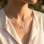 Woman wearing a silver mama bird necklace with tiny baby bird charms on a delicate chain, photographed in warm sunlight. Minimalist family jewelry symbolizing motherhood, children, and love.