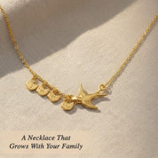 Gold mama bird necklace with four tiny baby bird charms engraved with initials, resting on soft linen fabric. Personalized family necklace symbolizing children and motherhood. Meaningful custom gift for mom.