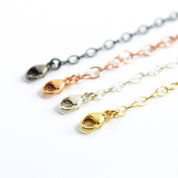 Close-up of necklace extenders in gold, silver, rose gold, and oxidized black, showcasing lobster clasp detail. Adjustable chain extension for necklaces and bracelets, adding 1–6 inches. Perfect minimalist jewelry accessory for everyday wear or gifting occasions.