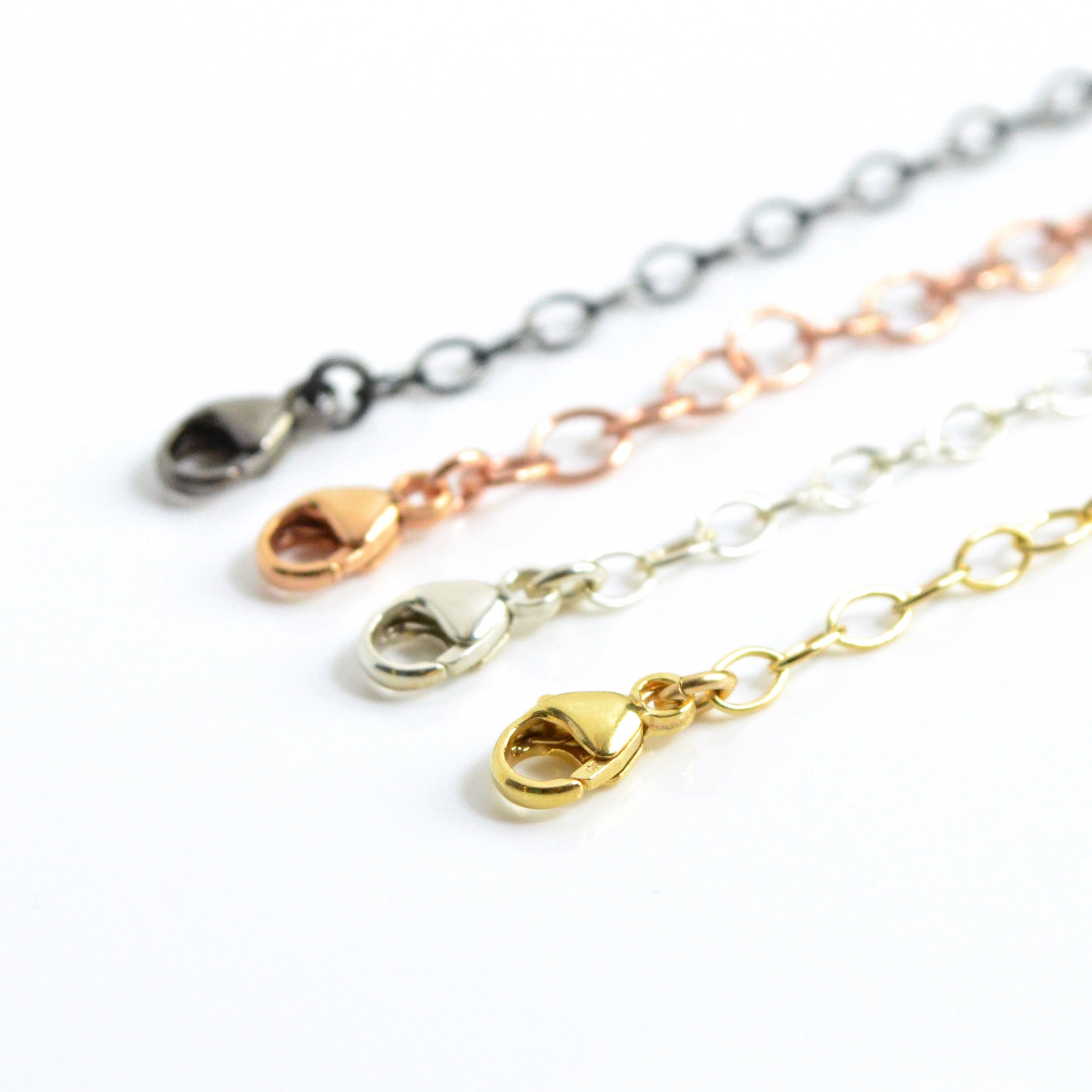 Close-up of necklace extenders in gold, silver, rose gold, and oxidized black, showcasing lobster clasp detail. Adjustable chain extension for necklaces and bracelets, adding 1–6 inches. Perfect minimalist jewelry accessory for everyday wear or gifting occasions.