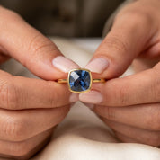 Kyanite ring held in hands showing faceted blue gemstone and bezel setting detail