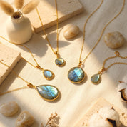 Round and teardrop natural labradorite pendant necklaces arranged on warm beige fabric in sunlight.