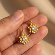 Close-up of gold floral birthstone earrings with faceted gemstone center, handmade bloom charm jewelry gift