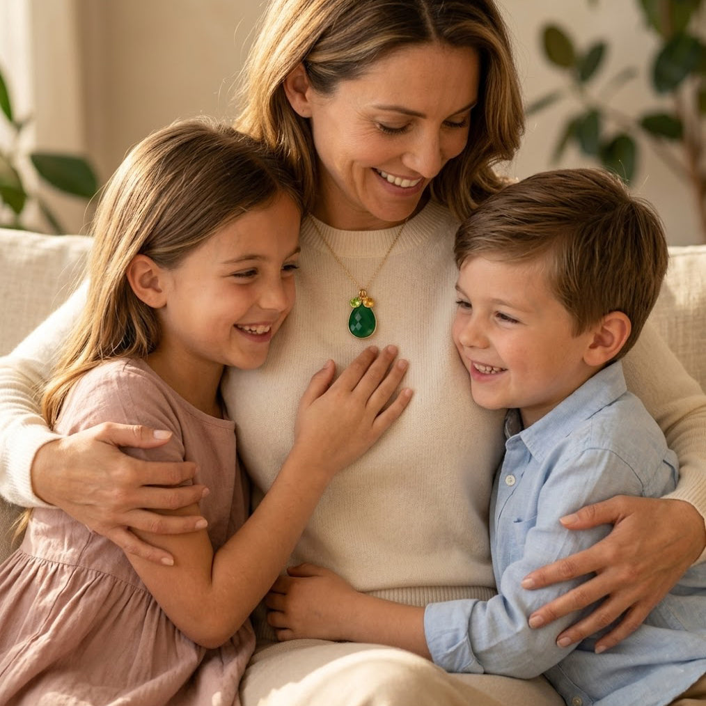 Mother wearing custom birthstone necklace while hugging her children at home