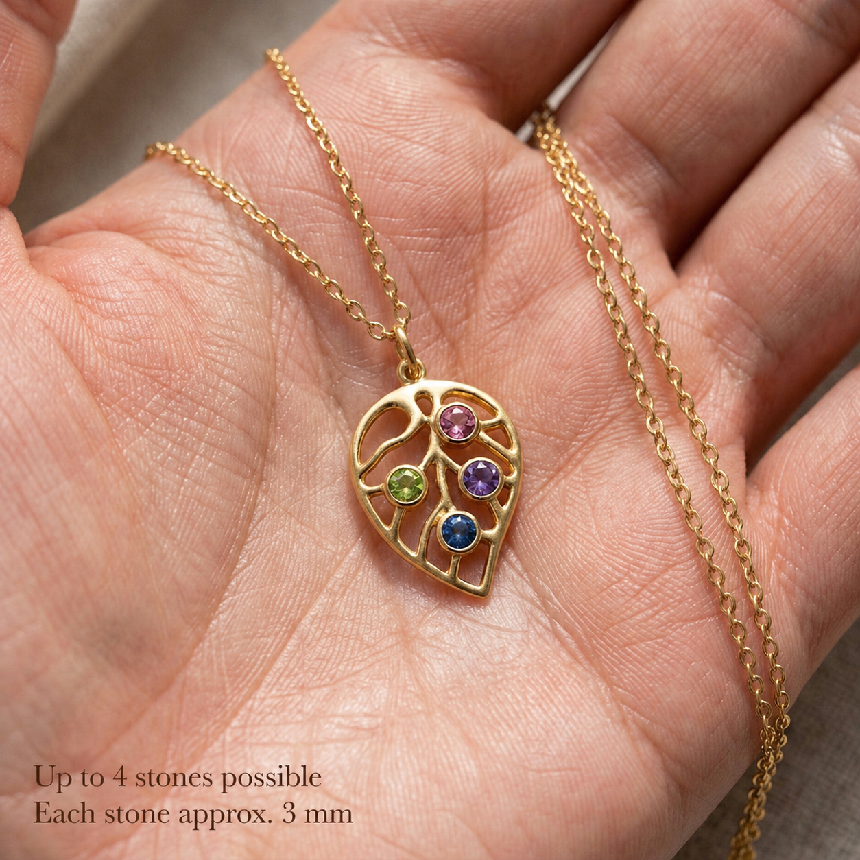 Close-up of custom leaf pendant necklace held in hand with four colorful birthstones, each stone approximately 3 mm.