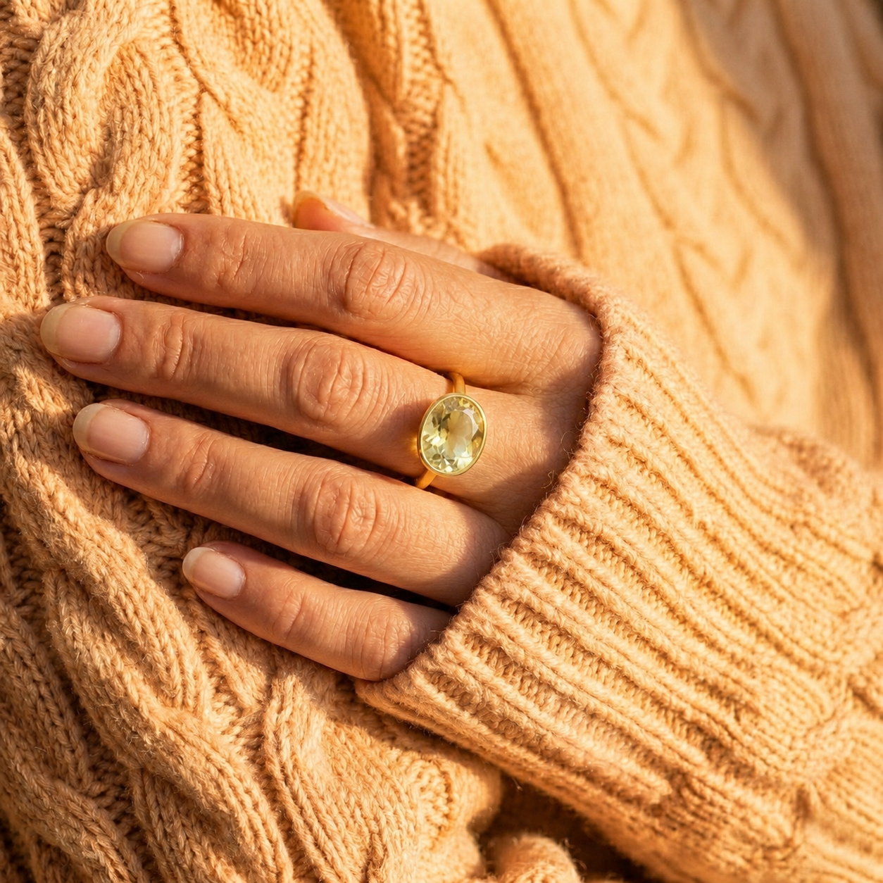Model wearing a lemon quartz oval ring with a soft peach sweater, showing the yellow gemstone ring styled on hand.