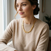 Woman wearing Gold geometric pyramid statement necklace with neutral sweater
