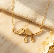 Gold personalized lovebirds necklace with two hand-stamped leaf initial charms on warm beige linen.