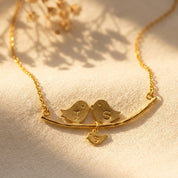 Gold lovebirds branch necklace with two parent birds and a dangling hand-stamped baby bird charm.