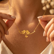 Woman wearing a gold personalized lovebirds family necklace with hand-stamped parent and baby bird initial charms.