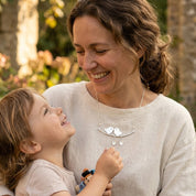 Mother and young daughter sharing a moment while the mother wears a silver family necklace.
