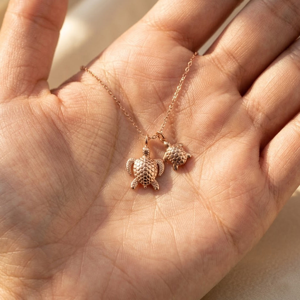 Mama turtle and baby turtle necklace held in hand, shown in rose gold finish as a meaningful gift for mothers and daughters.