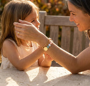 Custom family birthstone bangle bracelet worn by mom hugging her daughter, featuring engraved name disc charms and small faceted birthstones.