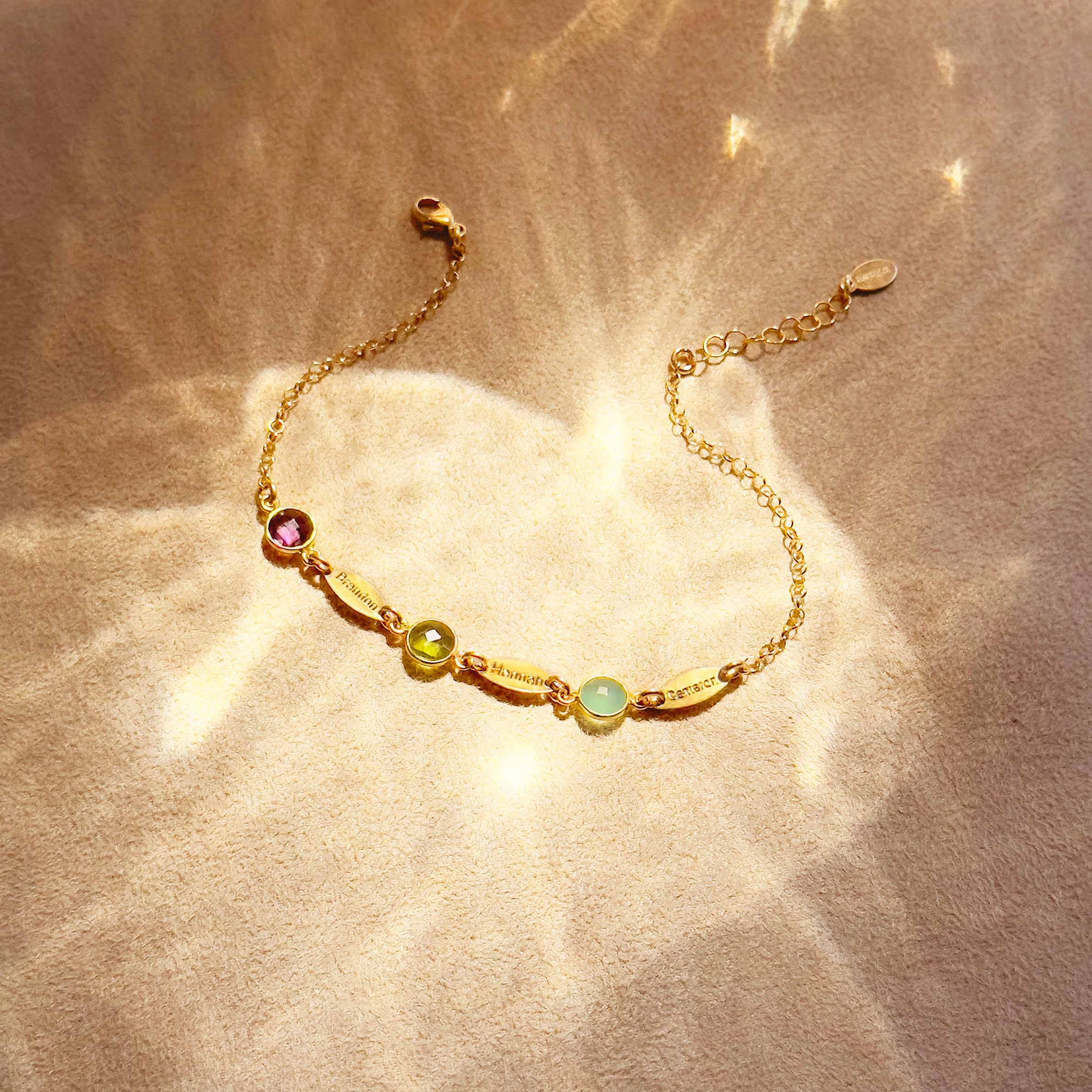 Close-up of custom birthstone name bracelet on wrist, personalized gold bracelet with engraved tags and colorful family birthstones