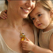 Mother wearing personalized birthstone necklace while holding her young child