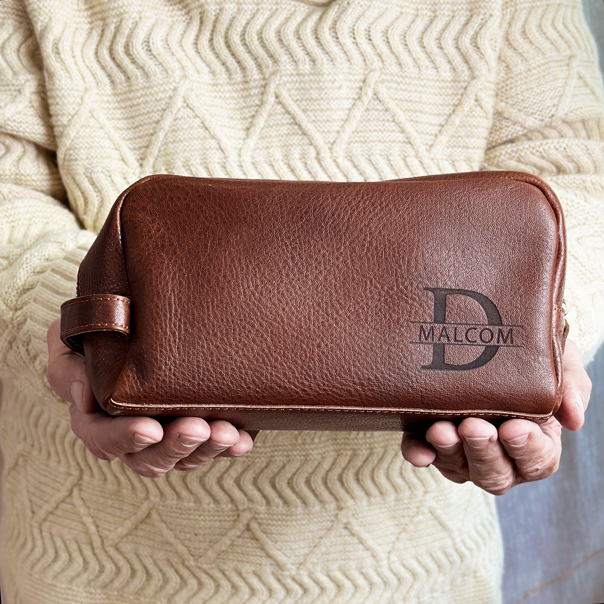 man holding customized toiletry bag with family monogram engraved. Custom engraved dopp kit, men's toiletry kit, personalized travel cosmetic bag, men's travel accessories, engraved men's toiletry bag, custom men's grooming bag, personalized dopp kit for men, stylish men's cosmetic bag, travel-friendly toiletry kit, unique men's travel gifts