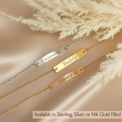 Three gold and silver name bracelets with engraved dog and cat names on a beige fabric background.