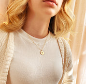 Model in beige top is wearing a custom Woman wearing a minimalist gold disc pendant necklace engraved with an actual paw print and pet name, a meaningful pet memorial jewelry piece for everyday wear, available in sterling silver, rose gold, or gold-filled, ideal sympathy gift for pet loss.