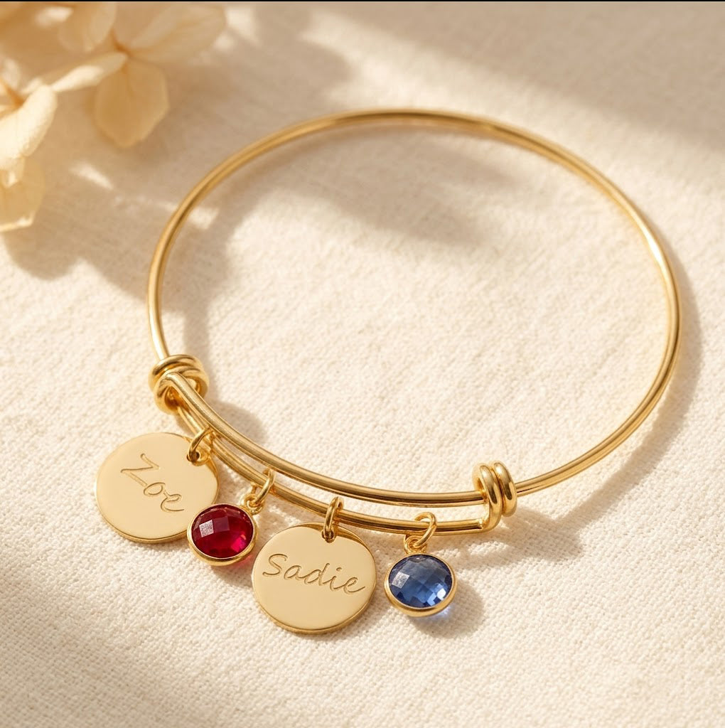 Gold bangle bracelet with engraved disks in handwriting script and garnet and kyanite birthstones. 