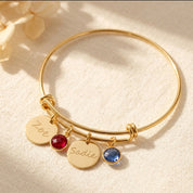 Gold bangle bracelet with engraved disks in handwriting script and garnet and kyanite birthstones. 