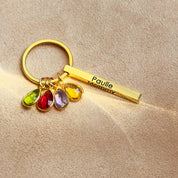 Gold personalized bar keychain for mom shown with four colorful teardrop birthstone charms representing each child. The slim 3D bar is laser-engraved with a name along the side, attached to a spring key ring for daily carry. A modern mom keychain that can be engraved on up to four sides with kids’ names, dates, or coordinates—an elegant family keychain keepsake for Mother’s Day or birthdays in a durable stainless steel finish.