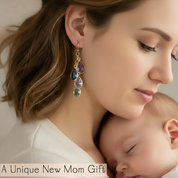 Woman wearing a gold earring with multicolored gemstones, holding a baby. Mother’s kids birthstone earrings featuring cascading gemstone drops in polished silver or gold tones, personalized to symbolize children or loved ones and designed as meaningful jewelry for special occasions.